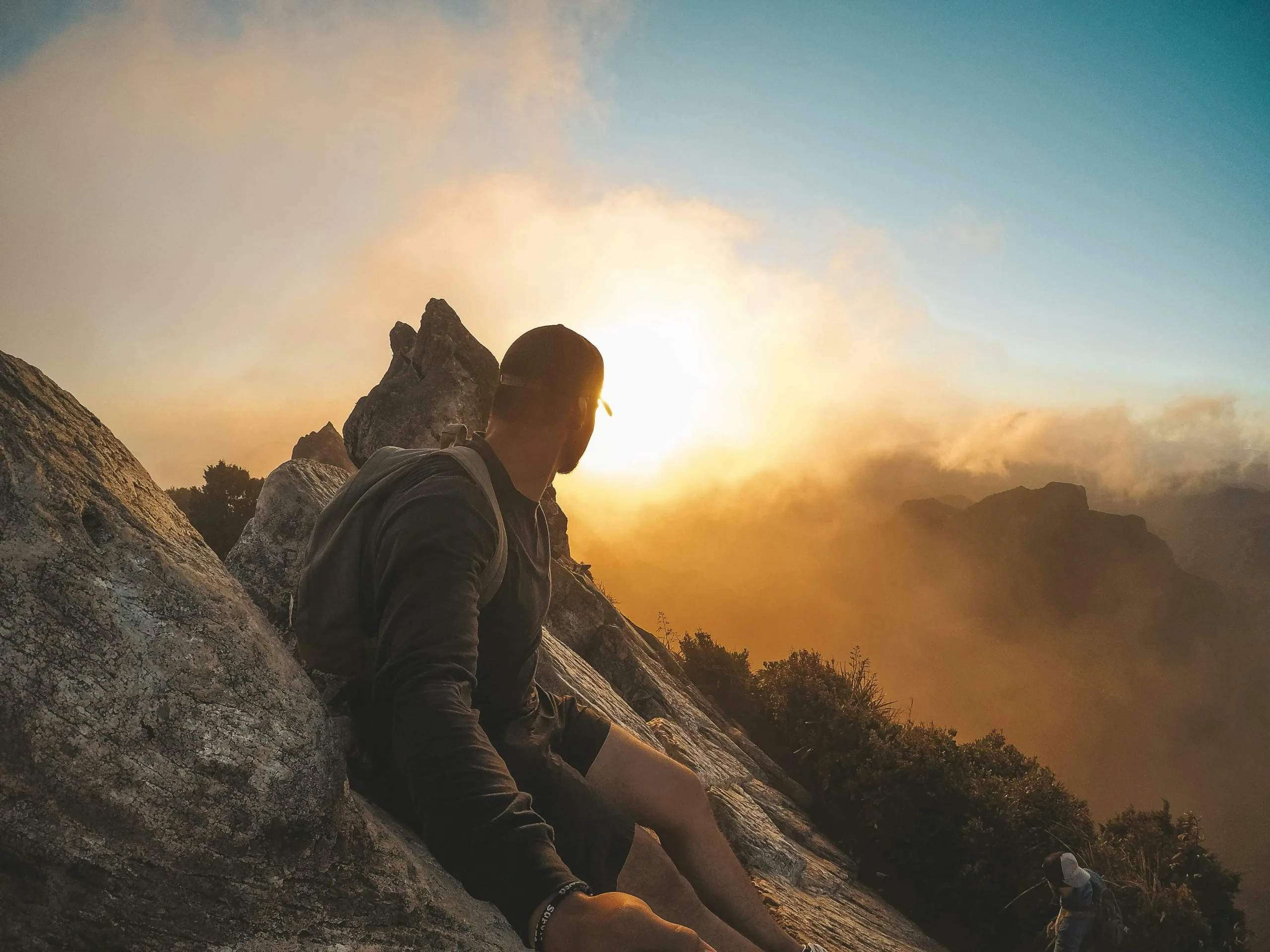 Man on a mountain overlooking a valley during a cloudy sunrise determined to continue on.