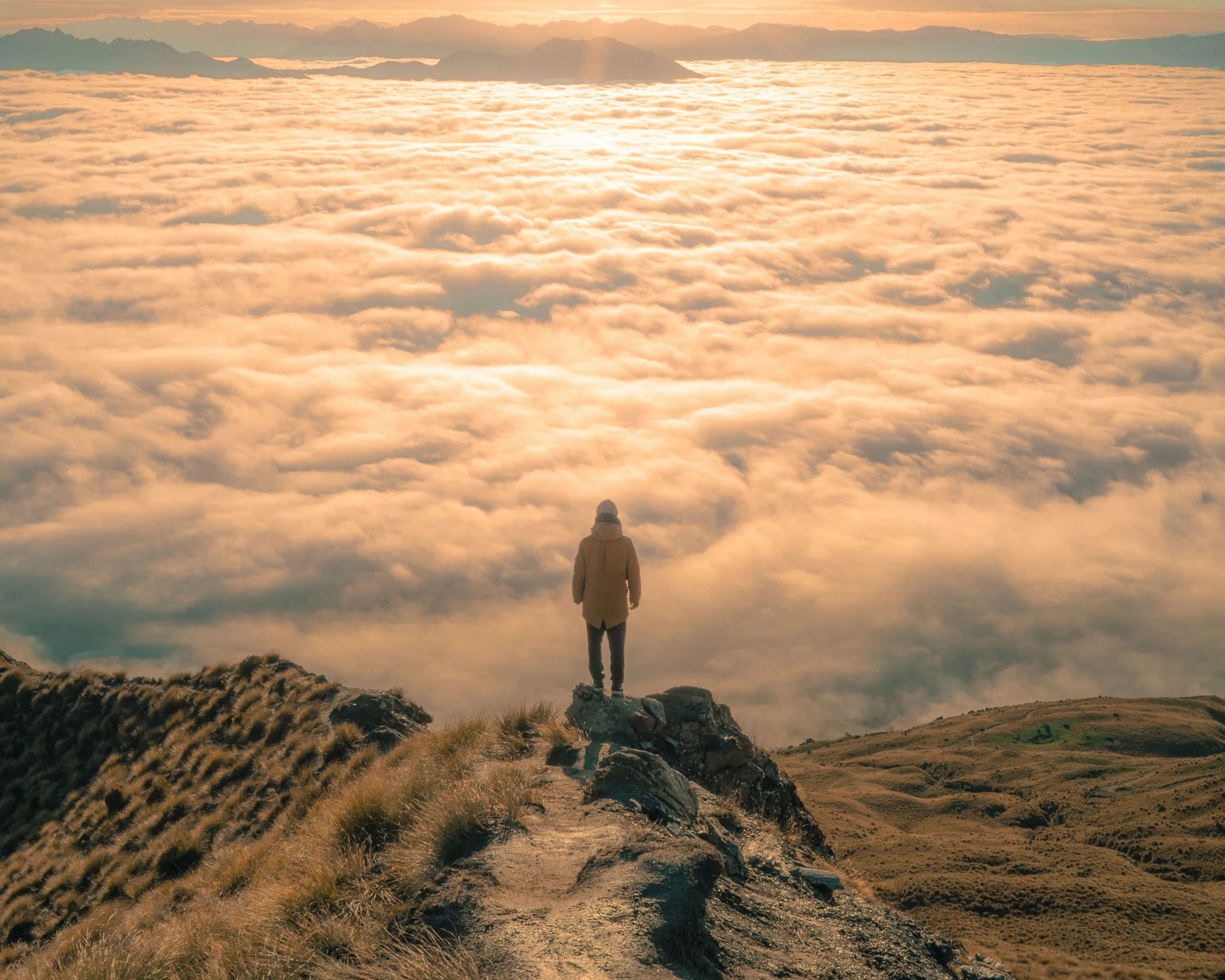 A silhouette of a person standing at the edge of a cliff or the top of a hill, gazing out into a vast landscape.