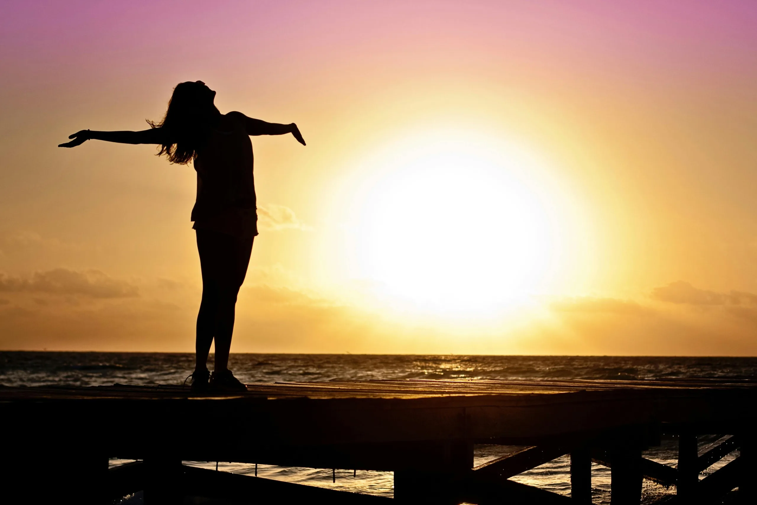 Woman standing on pier during sunrise feeling relieved.